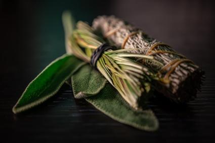 Fresh and dried sage native American smudging wiccan bundles with braided sweet grass herbs on a black wooden table surface