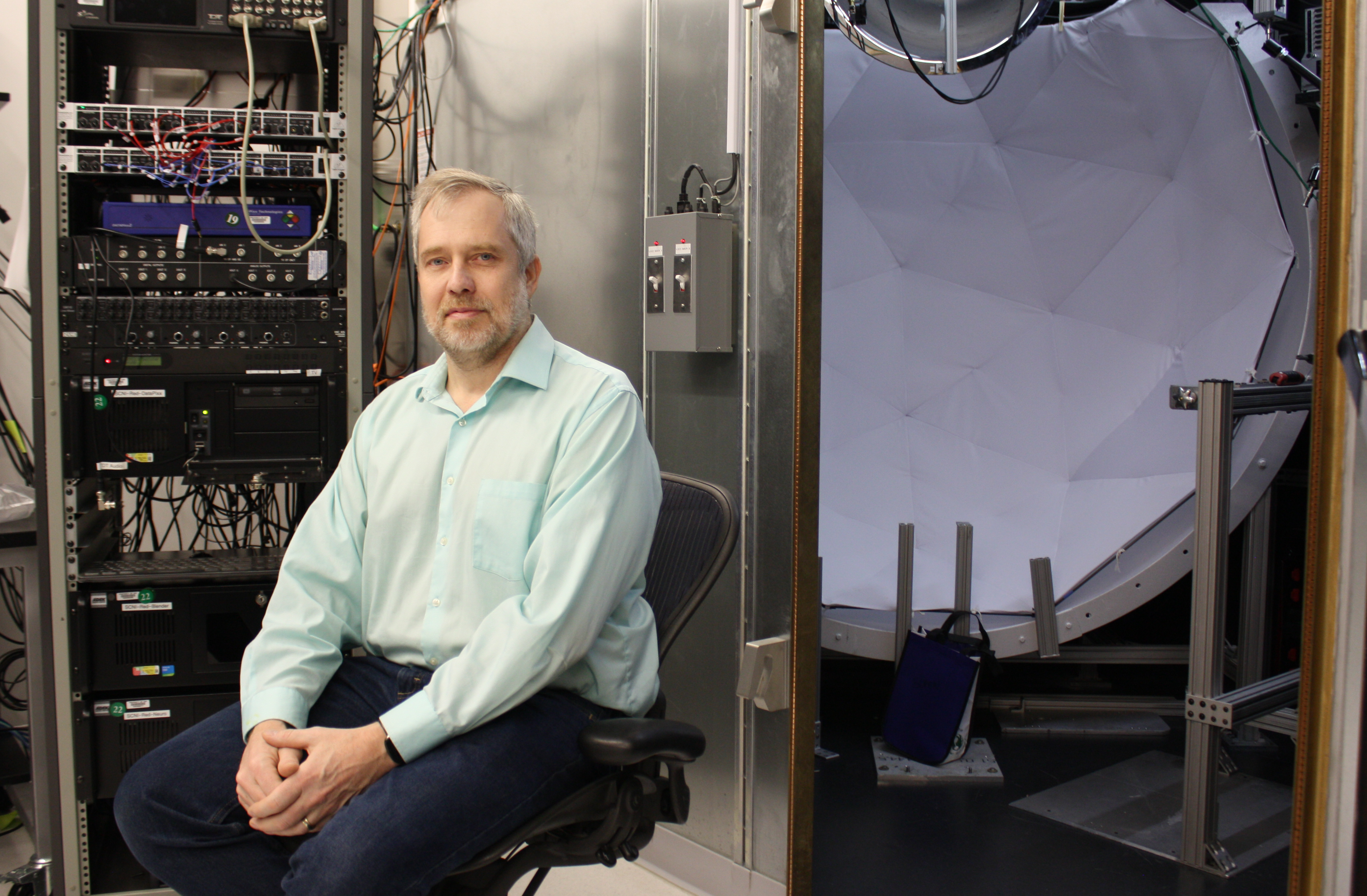 Dr. David Leopold sitting in front of an electrophysiology chamber equipped with a screen and projector.