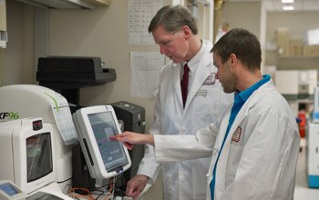 Drs. Crooks (right) and Linehan monitor output from the extracellular flux analyzer, a machine that measures metabolic changes such as oxygen consumption and glycolysis in cells.