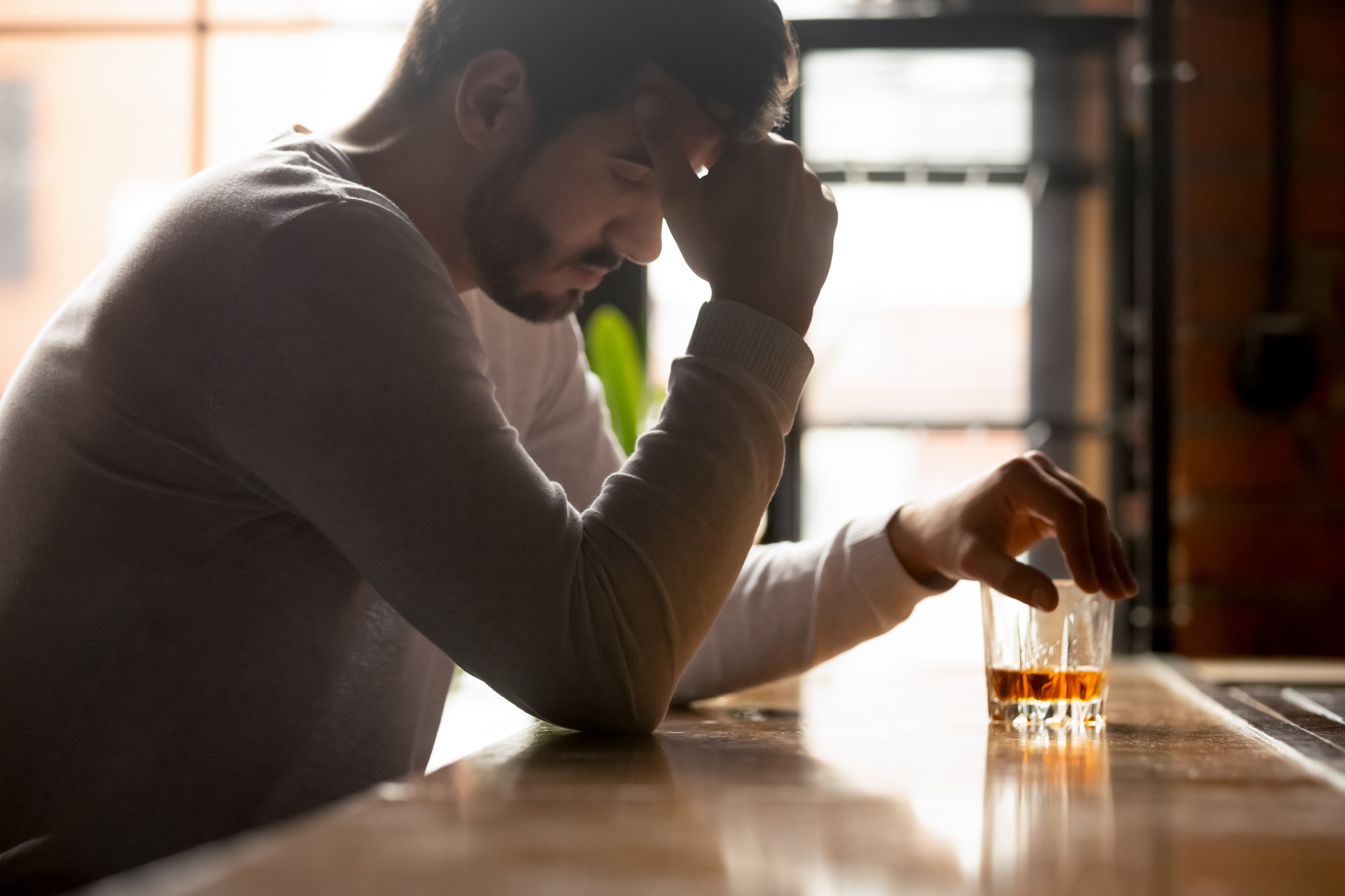 Man pondering over a whiskey drink at a bar.